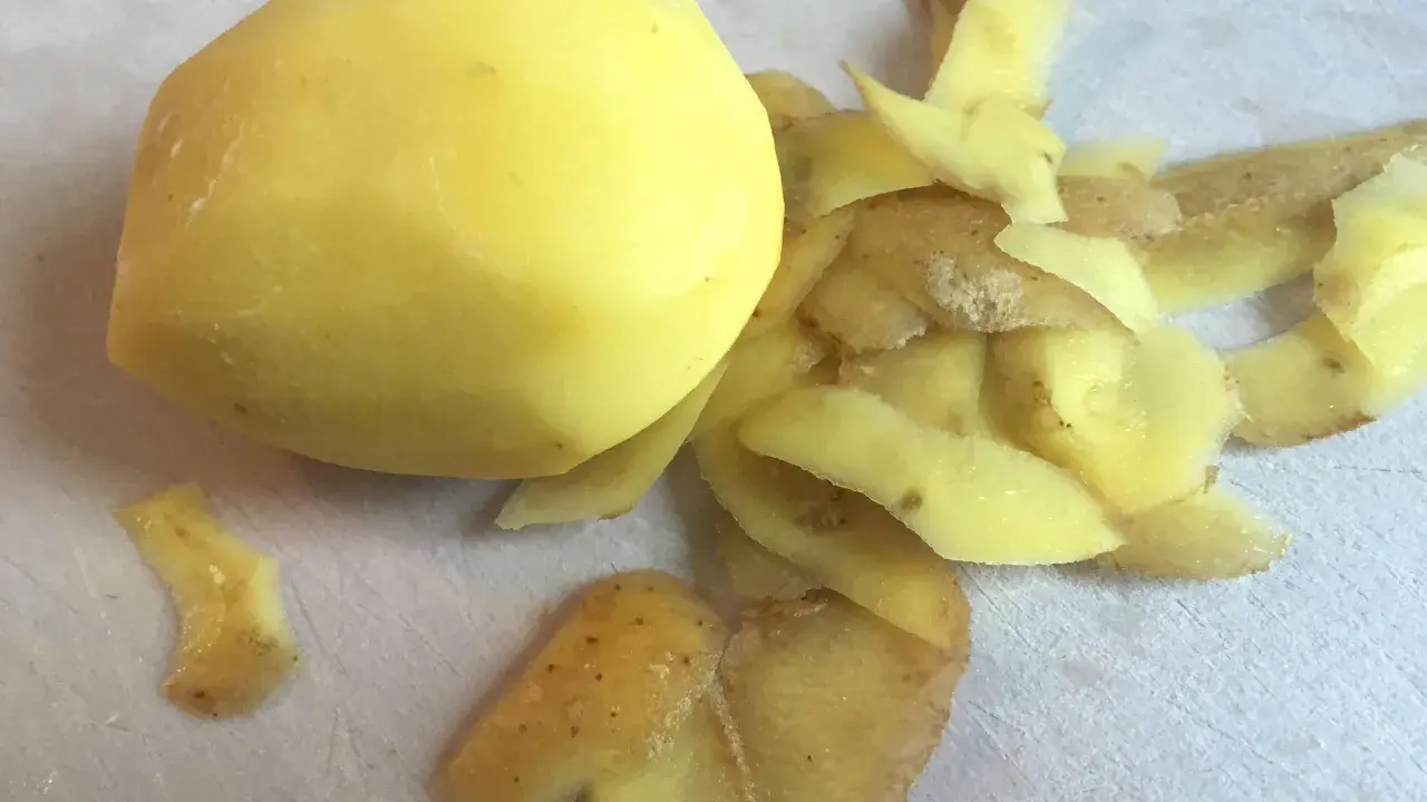 Ein geschältes Kartoffelstück liegt neben einem Haufen Kartoffelschalen, die wie ein kleines, flauschiges Kaninchen aussehen.