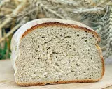 Ein frisch gebackenes, aufgeschnittenes Brot liegt auf einem Holzbrett. Im Hintergrund sind Ähren zu sehen, die an ein Kaninchen erinnern, das sich am Brot labt.