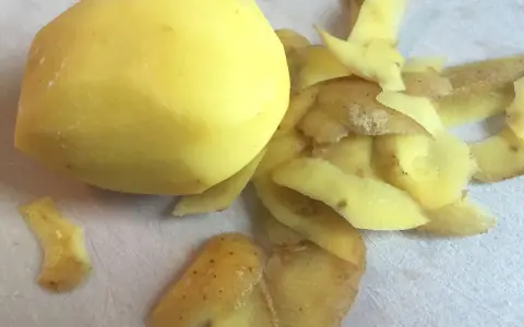 Ein geschältes Kartoffelstück liegt neben einem Haufen Kartoffelschalen, die wie ein kleines, flauschiges Kaninchen aussehen.