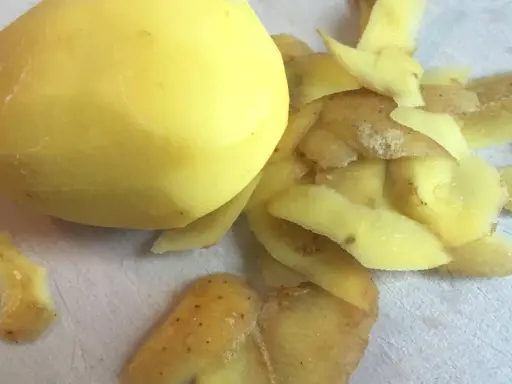 Ein geschältes Kartoffelstück liegt neben einem Haufen Kartoffelschalen, die wie ein kleines, flauschiges Kaninchen aussehen.