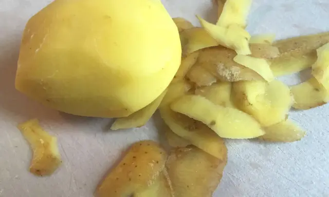 Ein geschältes Kartoffelstück liegt neben einem Haufen Kartoffelschalen, die wie ein kleines, flauschiges Kaninchen aussehen.